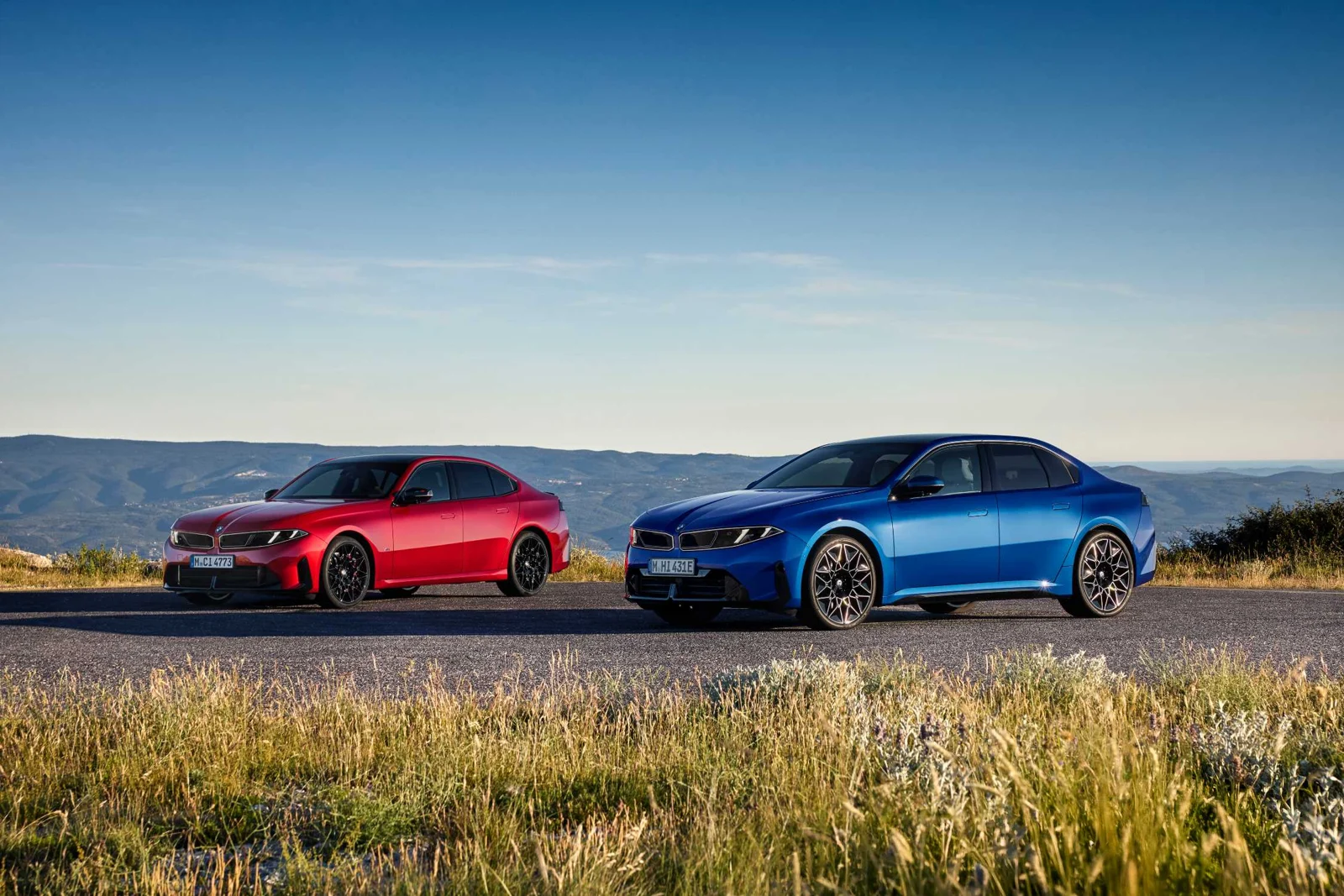Rdeča in modra limuzina nove BMW serije 3 ob cesti pred gorsko pokrajino