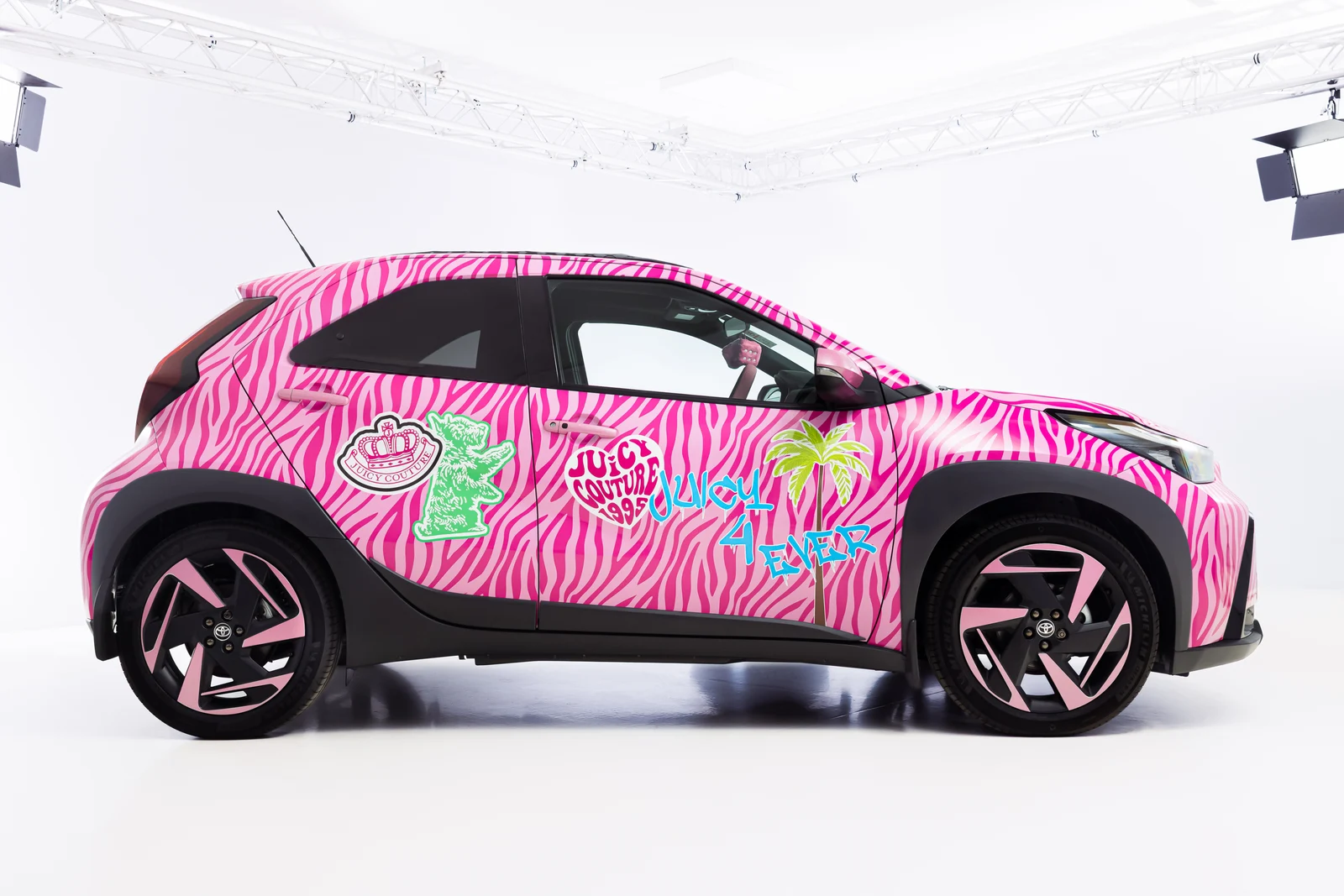Rožnata Toyota Aygo X Juicy Edition s pisano zebro in napisi na boku v fotografskem studiu