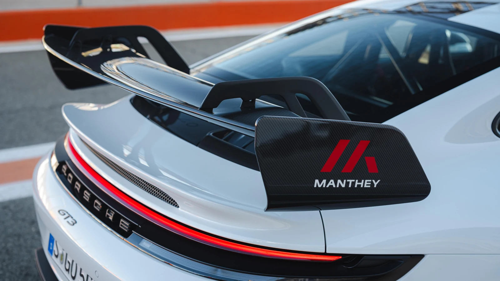 Zadnji del belega Porscheja 911 GT3 s karbonskim krilom Manthey ob dirkališču